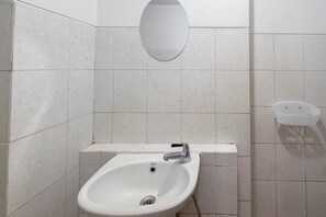 Kylpyhuoneessa on valkoinen pesuallas, peili ja pieni valkoinen hylly.