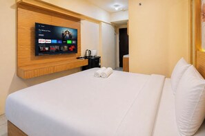 A hotel room with a bed, a TV mounted on the wall displaying a streaming service interface, and a small table with a kettle and cups. - Comfortable Good Vibes Studio Room At Suncity Residence Apartment (Sidoarjo)