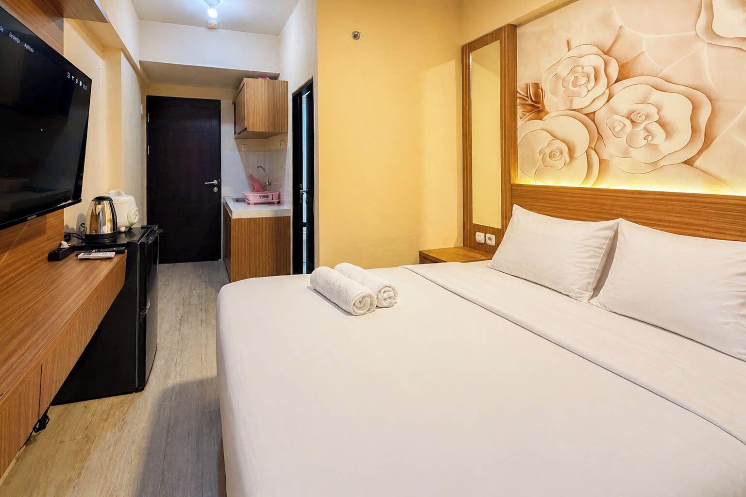 Habitación de hotel con cama, televisor, escritorio de madera, mesita de noche y pared con diseño floral.