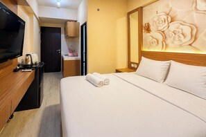 Hotellihuone, jossa on sänky, televisio, puinen työpöytä, yöpöytä ja kukka-aiheella koristeltu seinä.