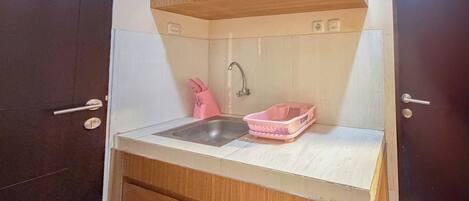 Une cuisine de taille réduite, avec un évier, un égouttoir à vaisselle rose et des placards en bois.