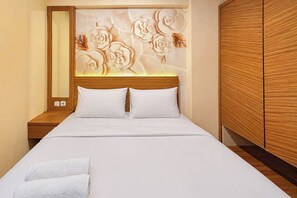 A hotel room with a bed, two pillows, a nightstand, a wooden headboard with floral carvings, and a wardrobe. - Comfortable Good Vibes Studio Room At Suncity Residence Apartment (Sidoarjo)