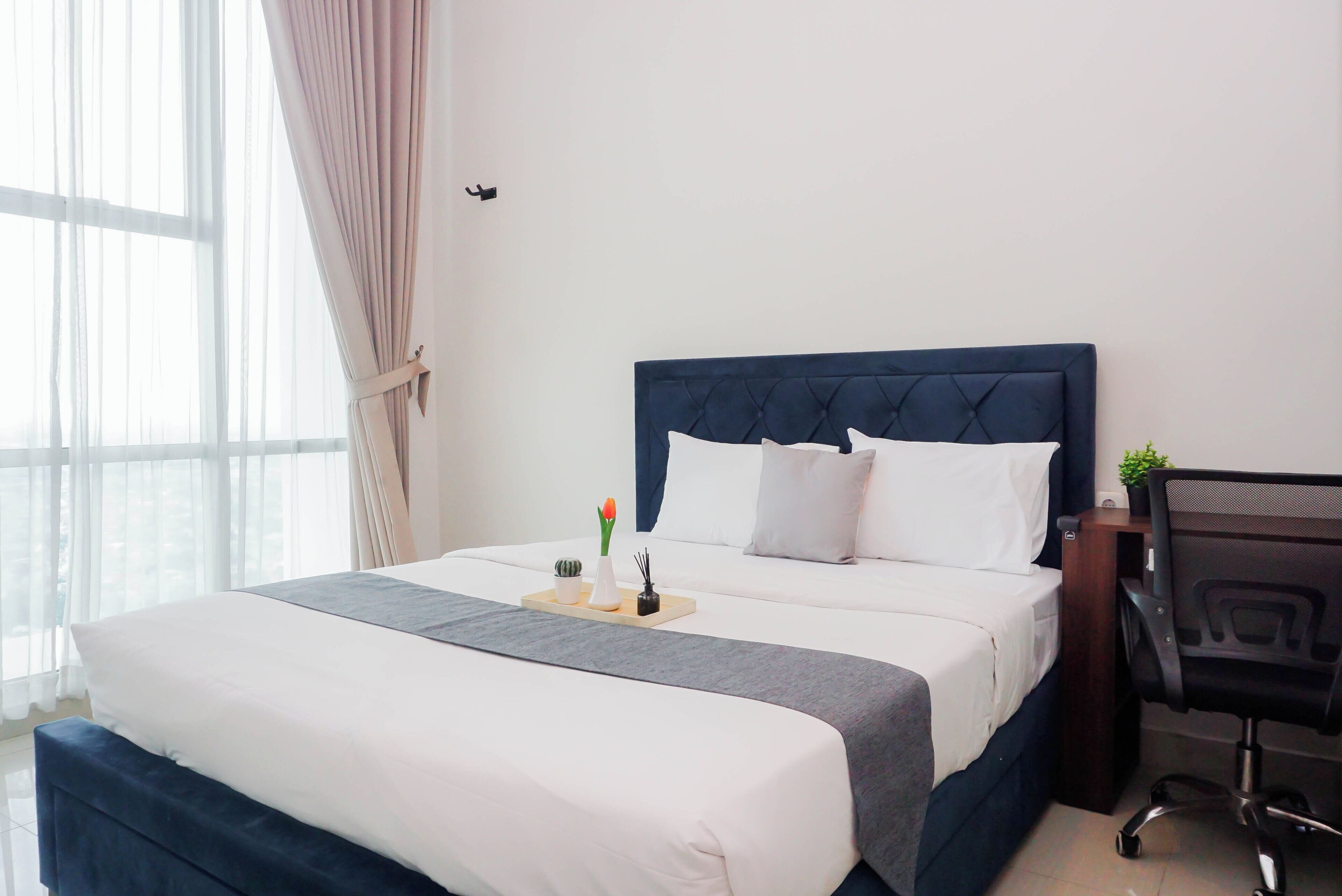 Una habitación de hotel con una cama grande, un escritorio y un ventanal con cortinas.