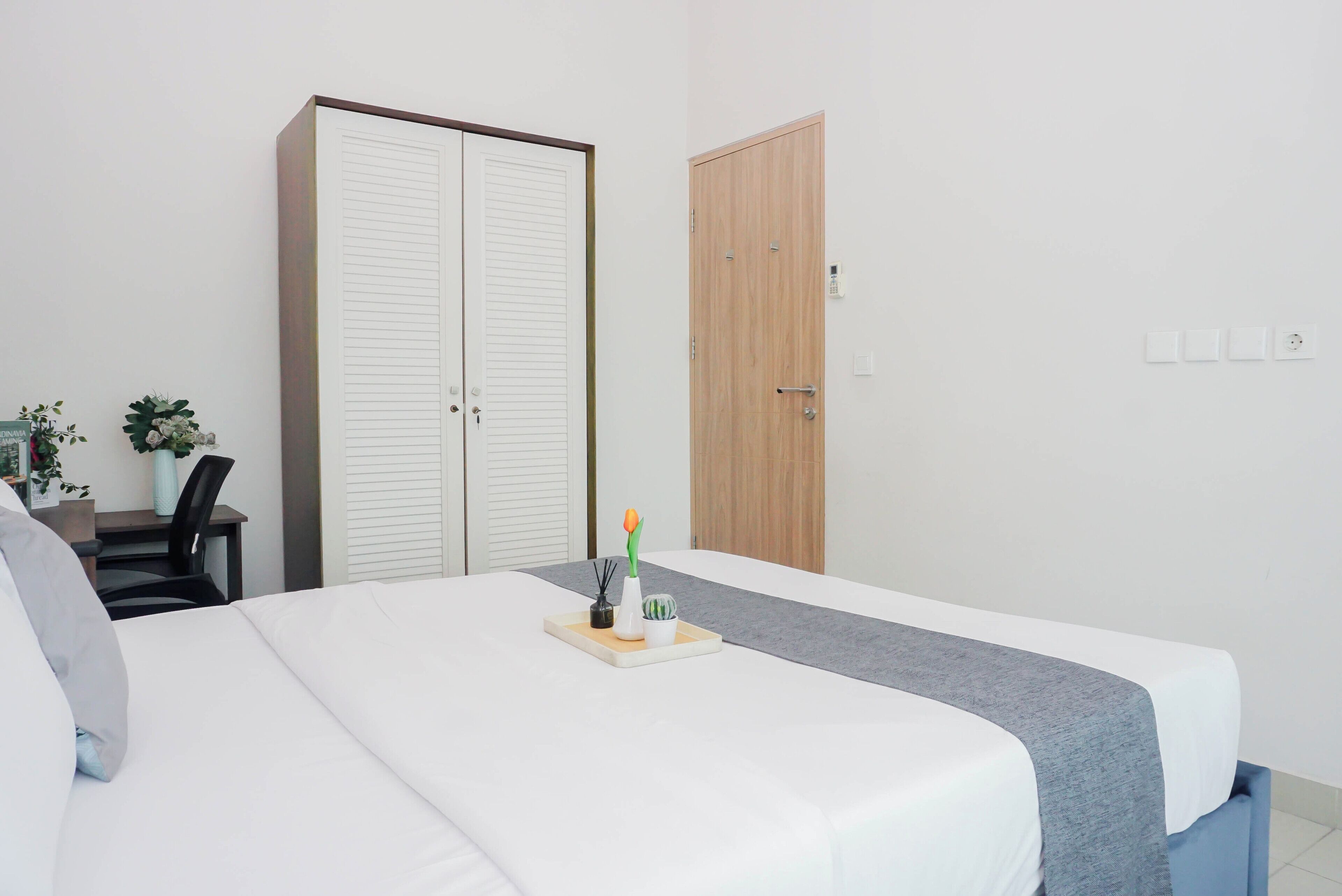 A hotel room with a bed, a desk, a chair, a wardrobe, and a door.