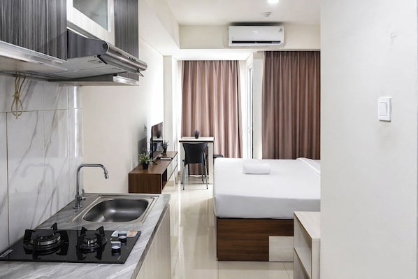 A compact hotel room with a kitchenette, a bed, a desk, and a bathroom.