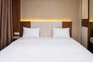 Hotellihuone, jossa on sänky, kaksi tyynyä, yöpöytä ja seinään kiinnitetty valaisin.