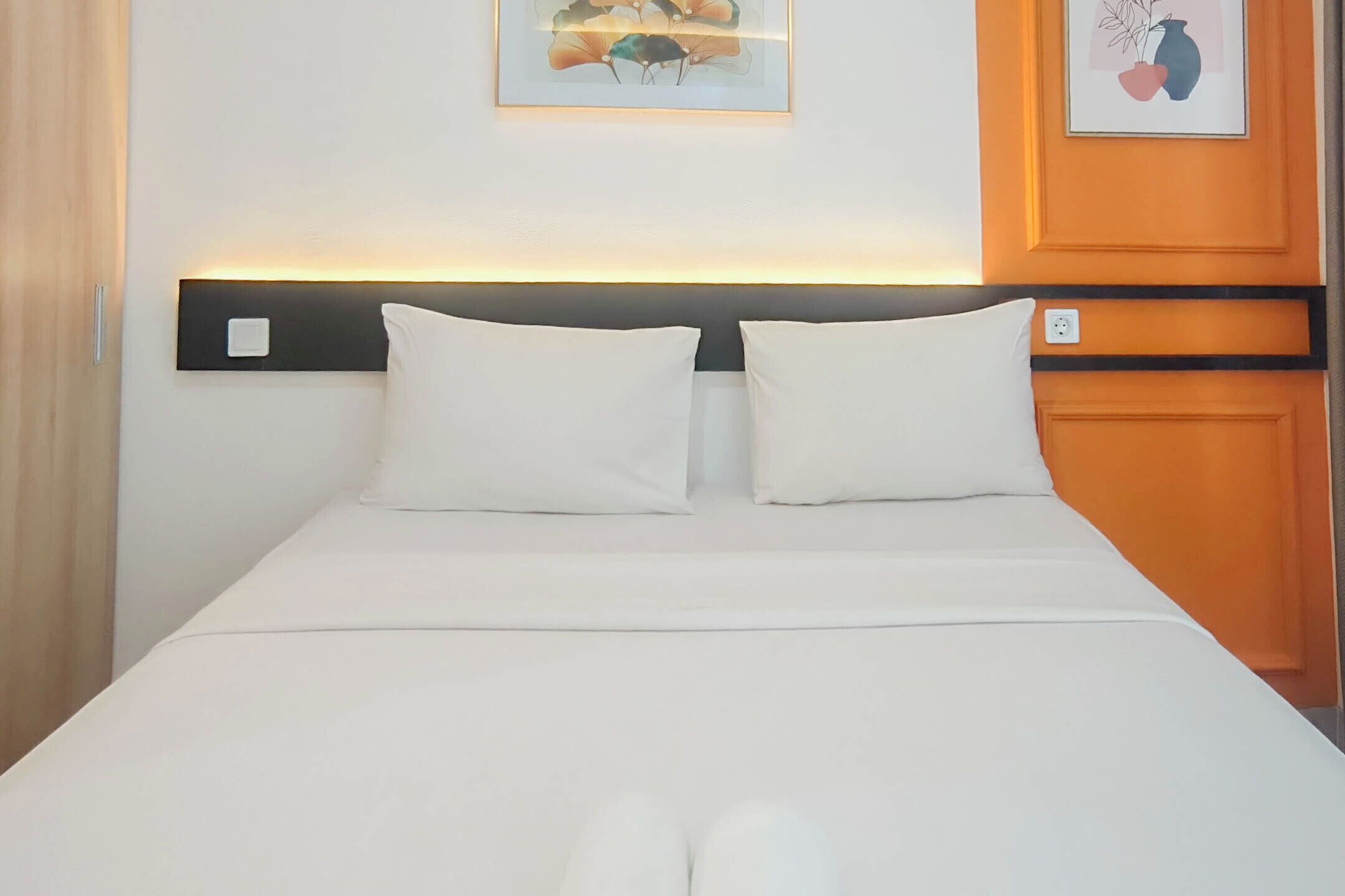 Een bed met witte beddengoed, een hoofdbord met een lichtbalk en twee ingelijste foto’s aan de muur.