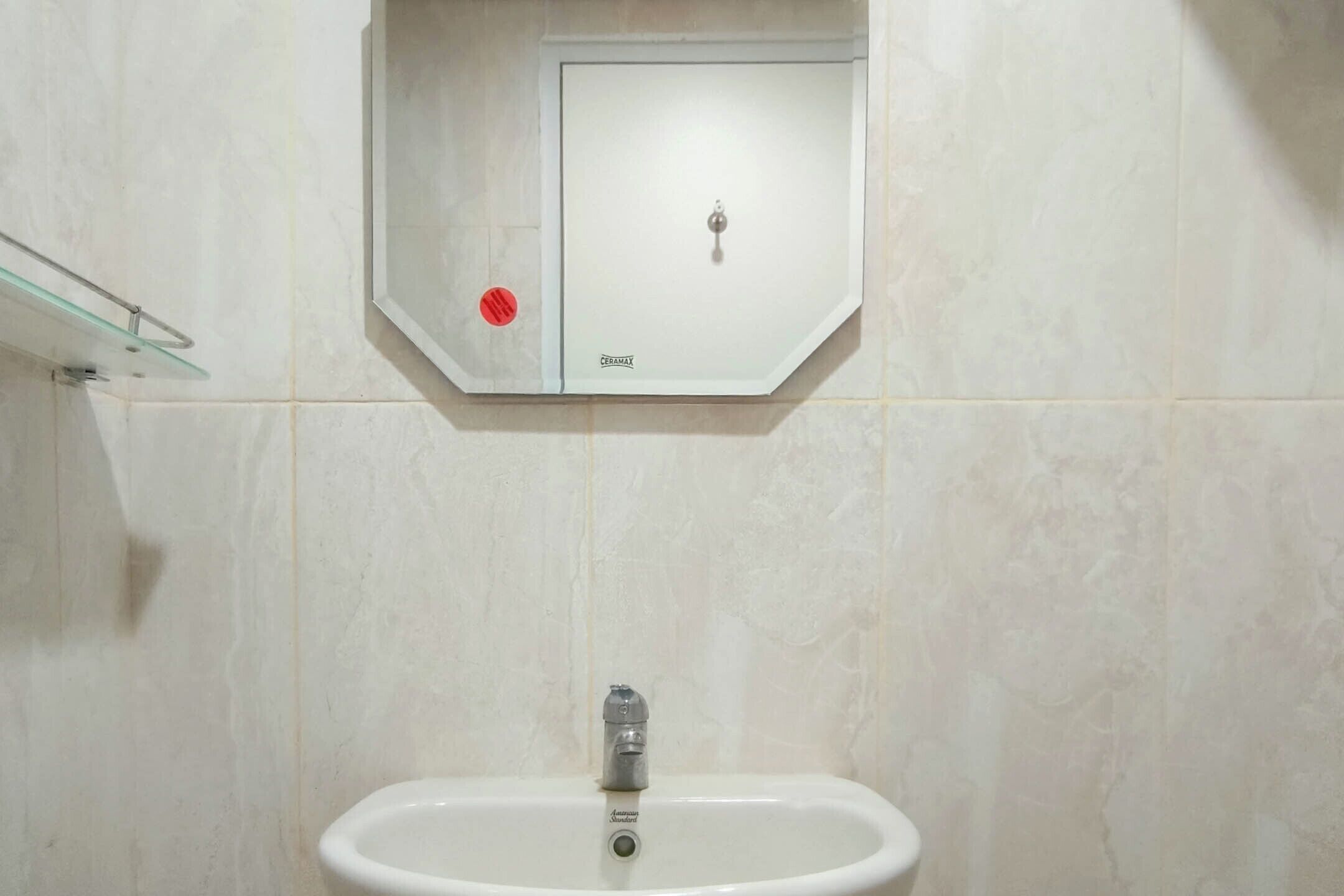 Un baño con un lavabo blanco, un estante de vidrio y un armario blanco con cerradura.