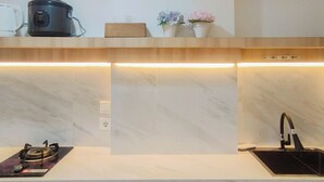 Une cuisine moderne dotée d’une cuisinière intégrée, d’un évier noir et d’un plan de travail sur lequel on trouve un cuiseur à riz et des objets décoratifs.