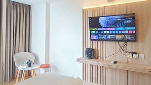A hotel room with a bed, a TV mounted on the wall, a small table with a chair, and a curtain.