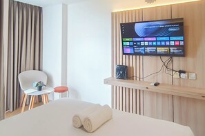 Habitación de hotel con una cama, televisión montada en la pared, una mesita con una silla y una cortina.
