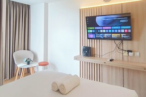 A hotel room with a bed, a TV mounted on the wall, a small table with a chair, and a curtain.