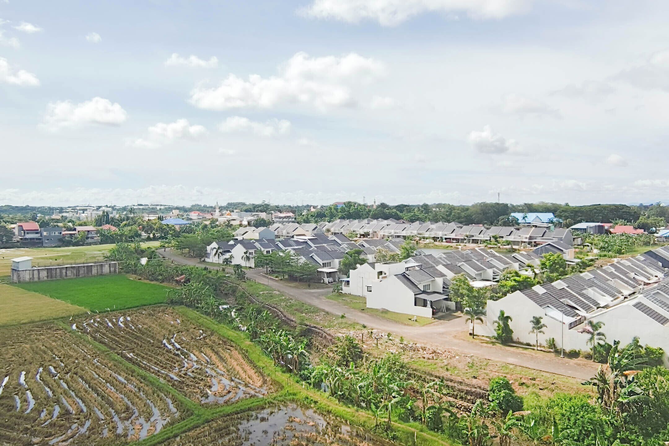 A residential area with houses arranged in rows, a large open field, and a distant view of a city skyline.