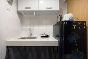 Una cocina compacta con un lavamanos, un refrigerador negro con diseño floral y una tetera en la encimera.