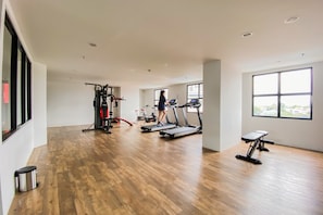 Un gimnasio con cintas de correr, una máquina de pesas y una banca.