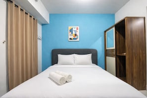 Habitación de hotel con cama, pared azul, armario de madera y una obra de arte geométrica.