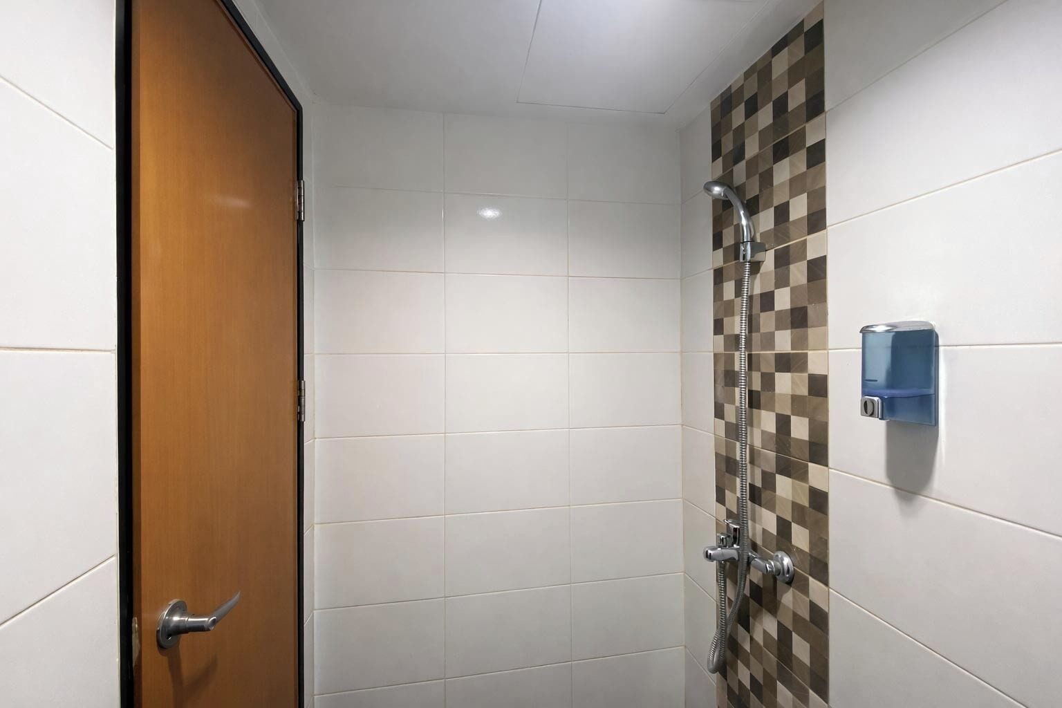 Un baño con azulejos blancos, una puerta de madera, una ducha con pared de baldosas de cuadros y un dispensador de jabón.
