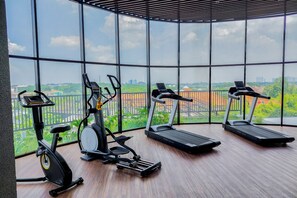 Ein Fitnessstudio mit drei Laufbändern, einem Crosstrainer und einem stationären Fahrrad, mit Blick auf die Stadt durch große Fenster.