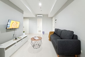 Un salon moderne avec un téléviseur à écran plat, une table basse ronde, un canapé gris et une console blanche.