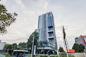 Un grand immeuble moderne, avec une façade en verre incurvée, entouré de verdure et surplombant un ciel dégagé.