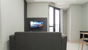 Una sala moderna con un sofá gris, un televisor de pantalla plana montado en la pared y un balcón con vistas.