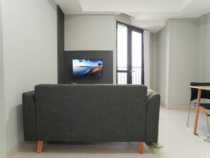 Una sala moderna con un sofá gris, un televisor de pantalla plana montado en la pared y un balcón con vistas.