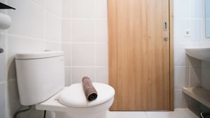 Un bany amb un vàter, una porta de fusta i un lavabo blanc.