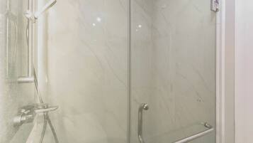 A glass-enclosed shower with a handrail, a wall-mounted faucet, and a control panel.