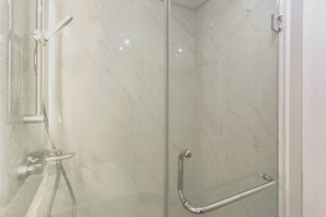A glass-enclosed shower with a handrail, a wall-mounted faucet, and a control panel. - Good Deal Studio With Modern Classic Style At The Vertu Apartment (Surabaya)