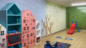 Een kinderspeelkamer met een blauw en roze speelhuisje, een glijbaan en diverse speelgoed.