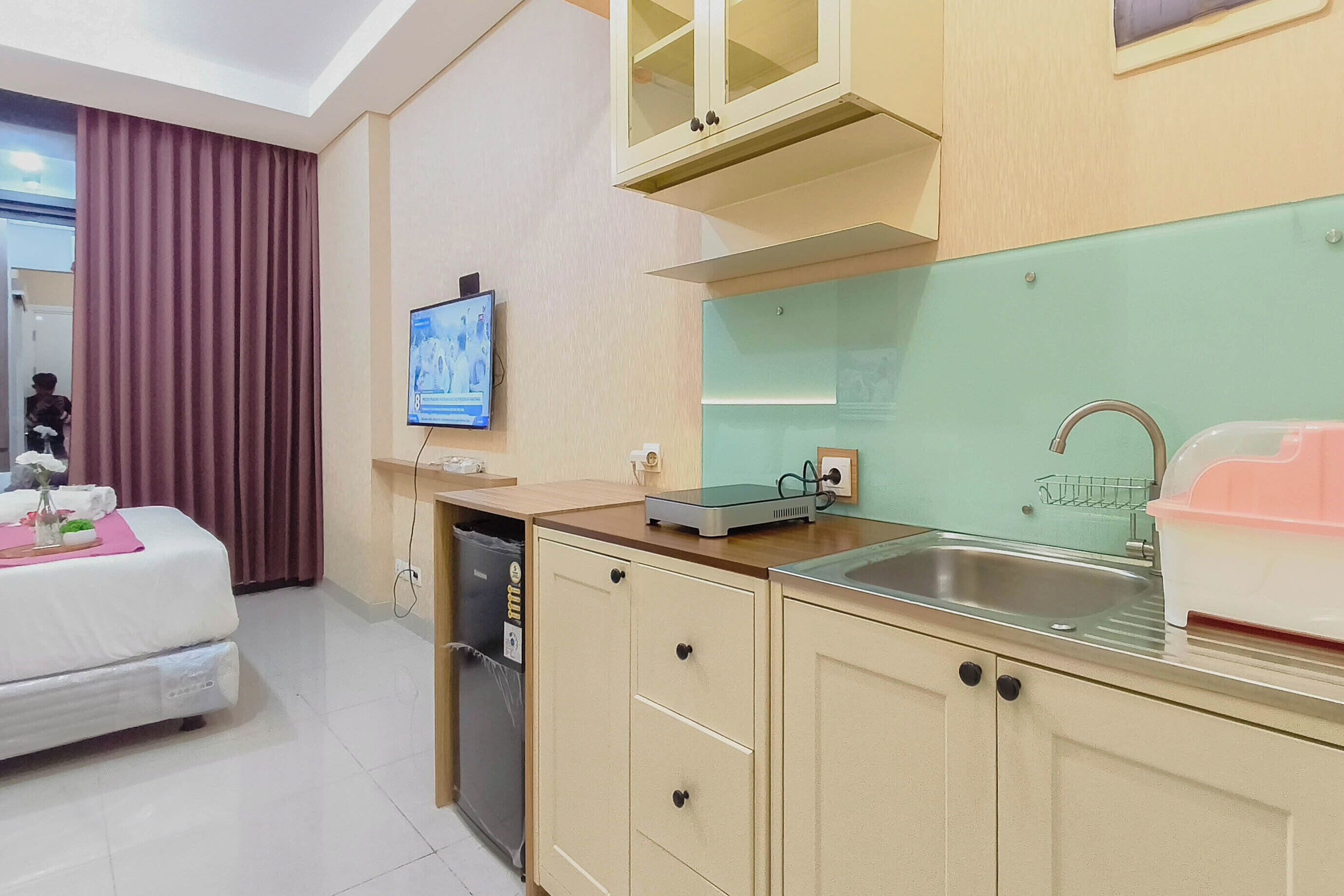 A hotel room with a bed, a television, a kitchen area with a sink, cabinets, and a window.