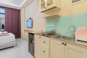 A hotel room with a bed, a television, a kitchen area with a sink, cabinets, and a window.
