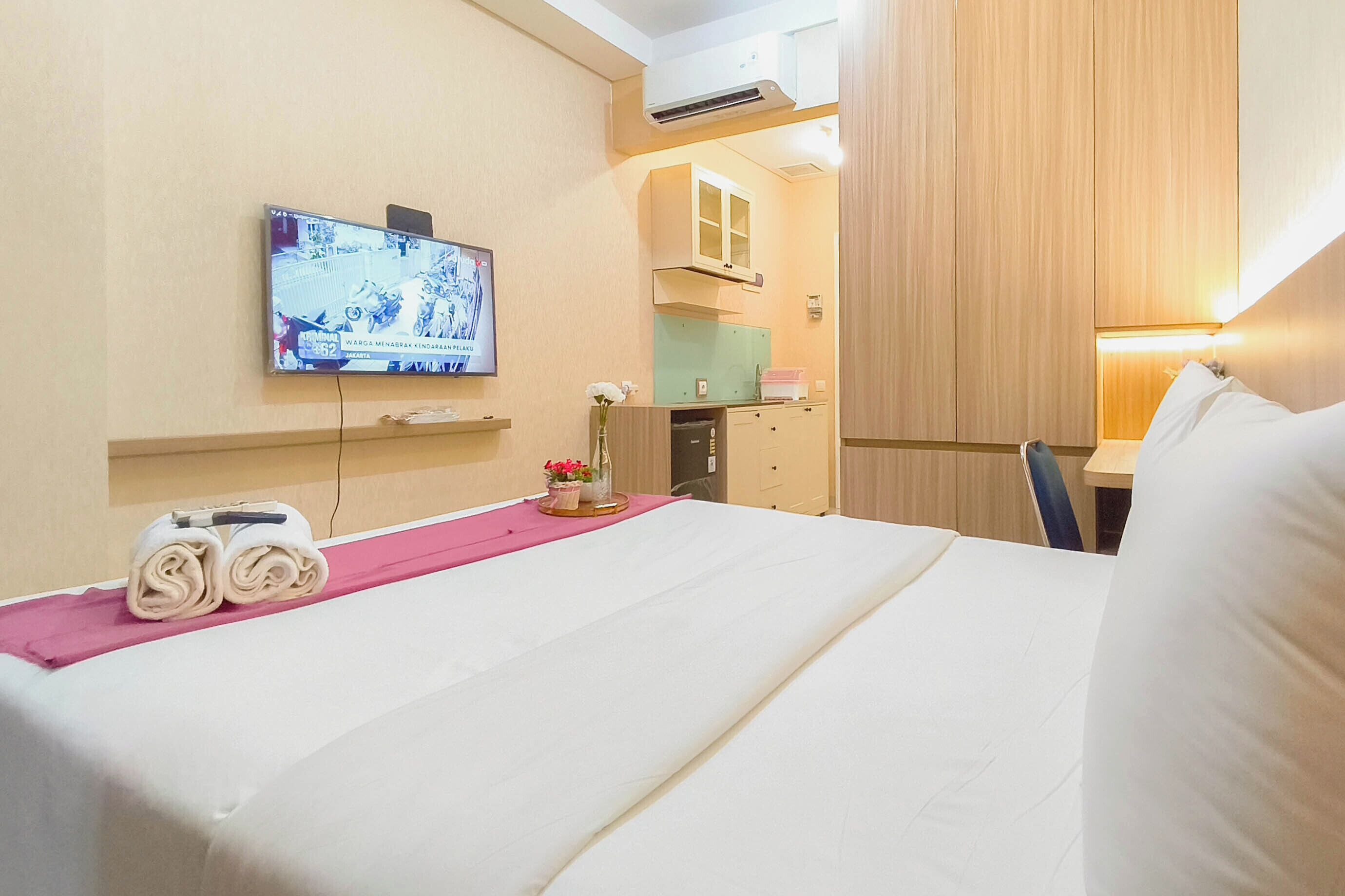Une chambre d’hôtel comprenant un lit, un téléviseur fixé au mur, un bureau avec une chaise et un petit coin cuisine.
