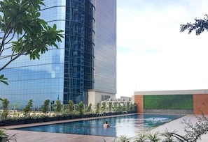 A swimming pool with a person in the water, surrounded by greenery and modern buildings.