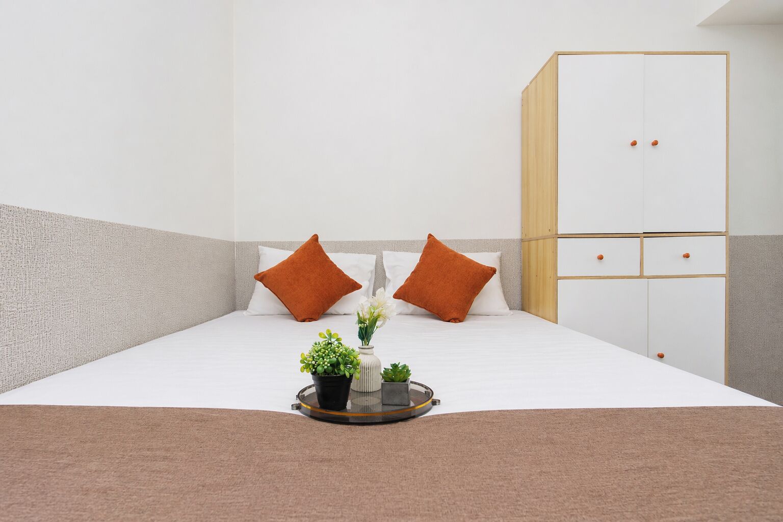 A neatly arranged bedroom with a bed, two pillows, a bedside table with a tray, and a wardrobe.