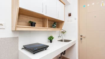 Cozinha moderna com armários brancos, prateleira de madeira, pia, bancada e um aparelho preto.
