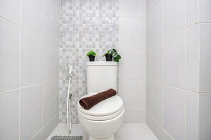 A bathroom with a toilet, a shower, and two potted plants on the toilet tank. - Compact Style Studio Apartment At Tokyo Riverside Pik 2 Near Nice (Teluknaga)