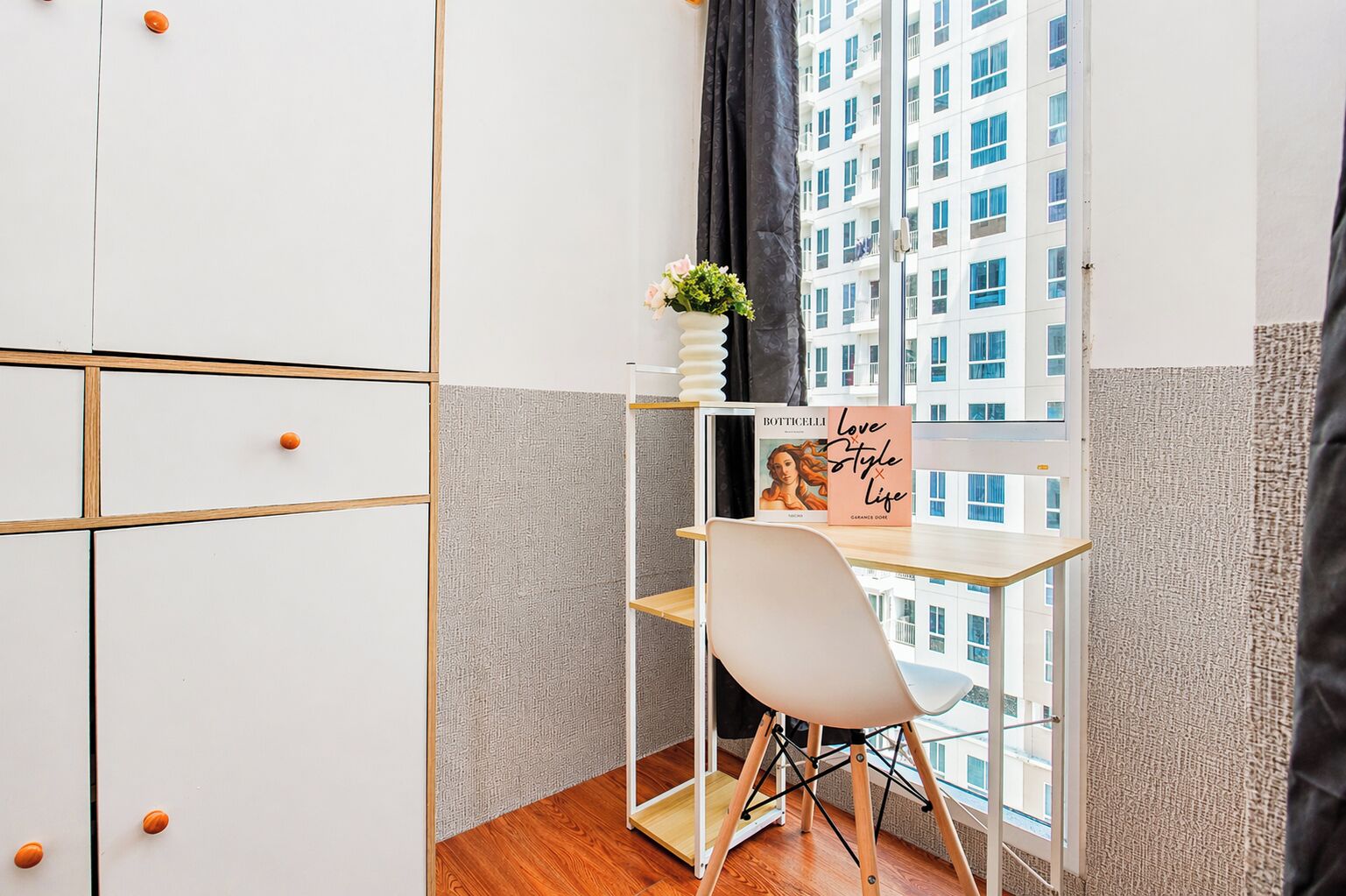 A small room with a desk, a chair, a window with a view of a building, and a decorative item on the desk.