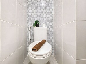 A bathroom with a white toilet, a small potted plant, and a rolled towel on the seat. - Studio Room Apartment At Tokyo Riverside Pik 2 Near Nice (Teluknaga)
