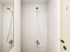 A bathroom with white tiled walls, a shower with a handheld showerhead, and a wall-mounted faucet.