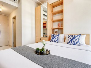 A hotel room with a bed, a bedside table with a tray of plants, a mirror, and a wooden shelving unit.