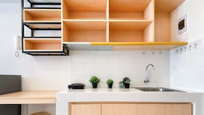 A modern kitchen with a white countertop, wooden cabinets, a built-in shelf, a sink, and a small stool. - Studio Room Apartment At Tokyo Riverside Pik 2 Near Nice (Teluknaga)
