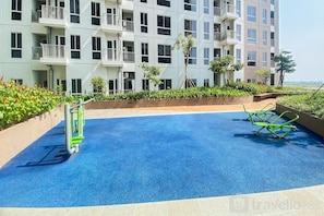 Una piscina en la azotea con suelo azul, rodeada por un muro bajo con vegetación y un edificio al fondo.