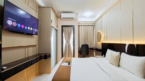 A hotel room with a bed, a TV mounted on the wall, a desk, and a chair. - Warm And Restful Studio Room At Apartment Transpark Bintaro (South Tangerang)
