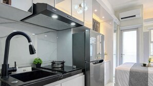 A modern kitchen with a black faucet, stainless steel appliances, and a marble countertop. - Comfy White Studio At Transpark Juanda Bekasi Timur Apartment (Bekasi)
