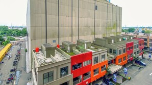 A multi-story building with a flat facade, a parking lot with several vehicles, and a clear view of the surrounding urban landscape. - Comfy White Studio At Transpark Juanda Bekasi Timur Apartment (Bekasi)