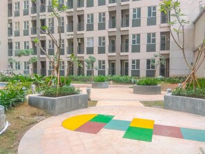 A multi-story residential building with balconies, surrounded by landscaped gardens and a colorful pavement design.
