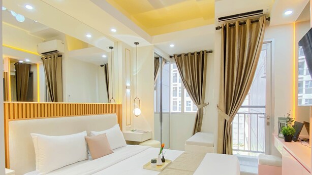 A modern hotel room with a large bed, bedside tables, a mirror, and a view of the outside. - Airy Studio Apartment At Transpark Juanda Bekasi Timur (Bekasi)