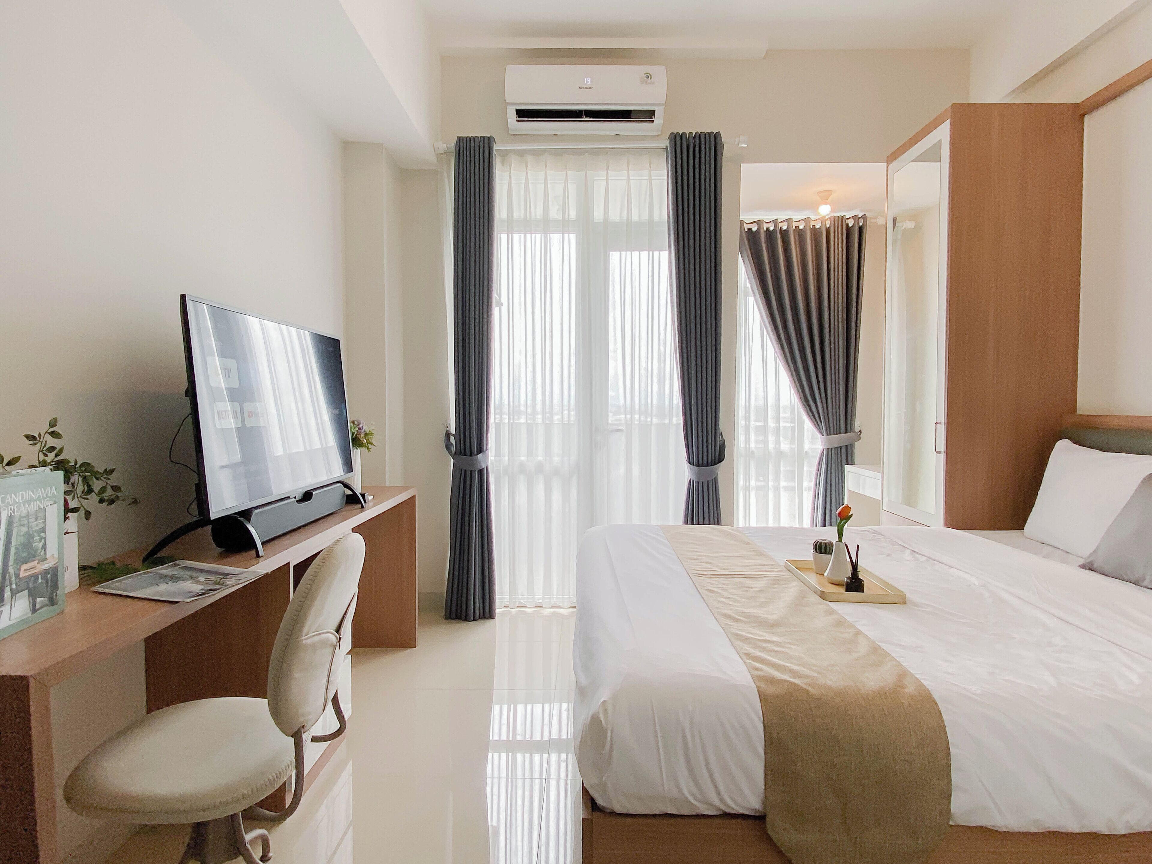 A hotel room with a bed, a desk with a computer, a chair, and an air conditioning unit.