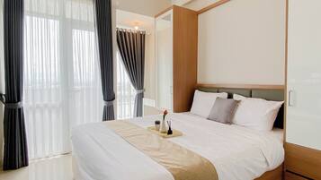 A hotel room with a large bed, a bedside table, a nightstand, a window with curtains, and an air conditioning unit.